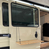 Klappbare Holzablage an einem Wohnmobilfenster, befestigt mit zwei schwarzen Seilen.