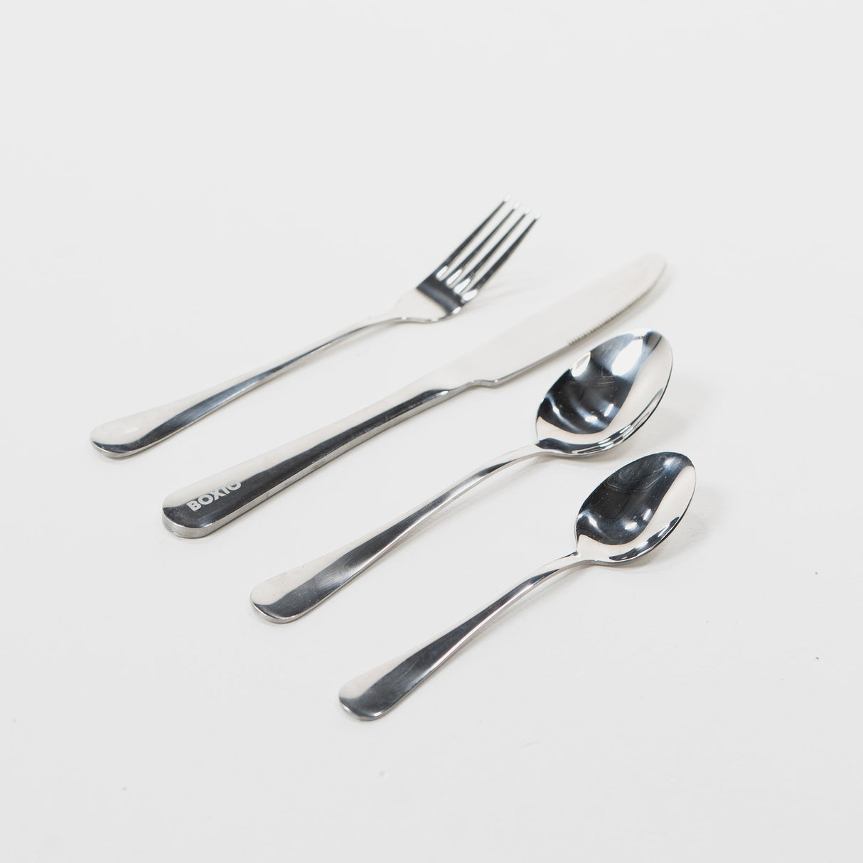 Edelstahlbesteckset mit Messer, Gabel und zwei Löffeln auf weißem Hintergrund.