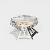 Sternförmiger Portable Grill aus Edelstahl mit Holzscheiten im Inneren, ideal für Camping und Outdoor-Aktivitäten.