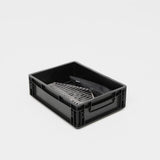 Schwarze Kunststoffbox mit einem Grillrost und einem schwarzen Deckel im Inneren.