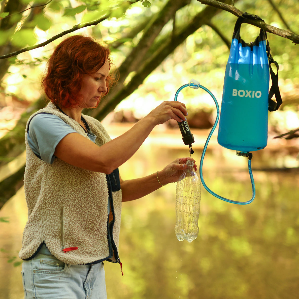 Frau füllt eine Wasserflasche mit einem Filter aus einem blauen Wasserbehälter in der Natur.