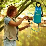 Frau füllt eine Wasserflasche mit einem Filter aus einem blauen Wasserbehälter in der Natur.