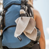 Grauer Handtuch aus Waffelstruktur hängt an einem blauen Rucksack, der von einer Person getragen wird.