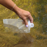 Eine Hand hält eine transparente Wasserflasche, während sie in einem klaren Gewässer steht.