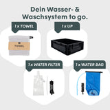 Wasser- und Waschsäule mit Handtuch, schwarzer Box, Wasserfilter und blauer Wasserbeutel zur Nutzung unterwegs.