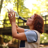Frau trinkt aus einer Flasche mit Wasserfilter in einem sonnendurchfluteten Wald.