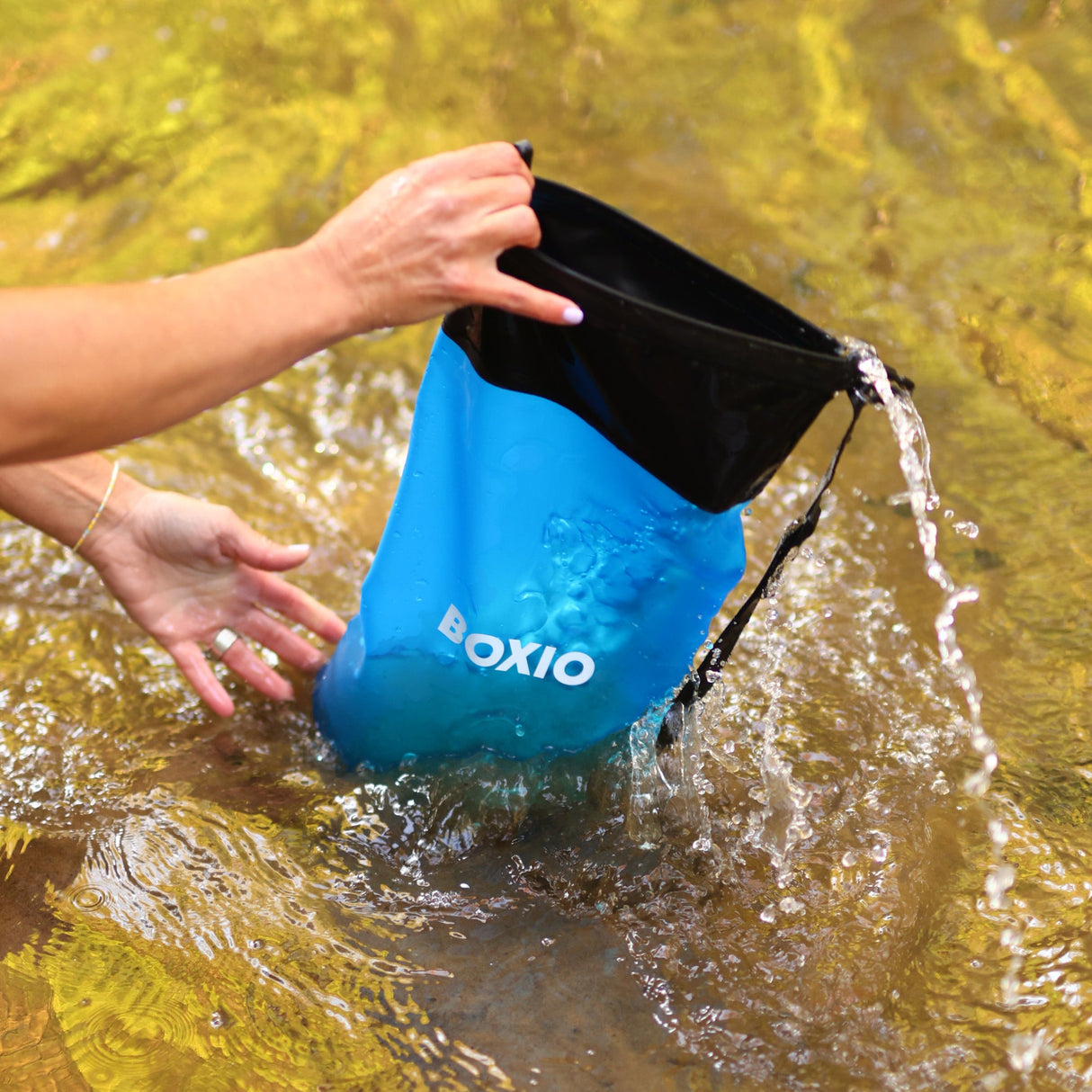 Eine Hand hält einen blauen wasserdichten Beutel, aus dem Wasser fließt, im klaren Wasser.